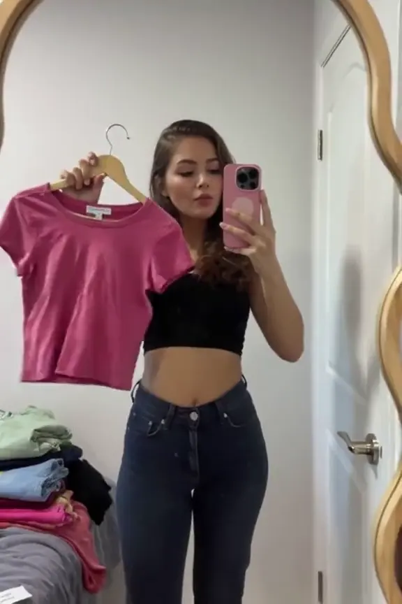 Woman filming a mirror selfie while comparing two tops